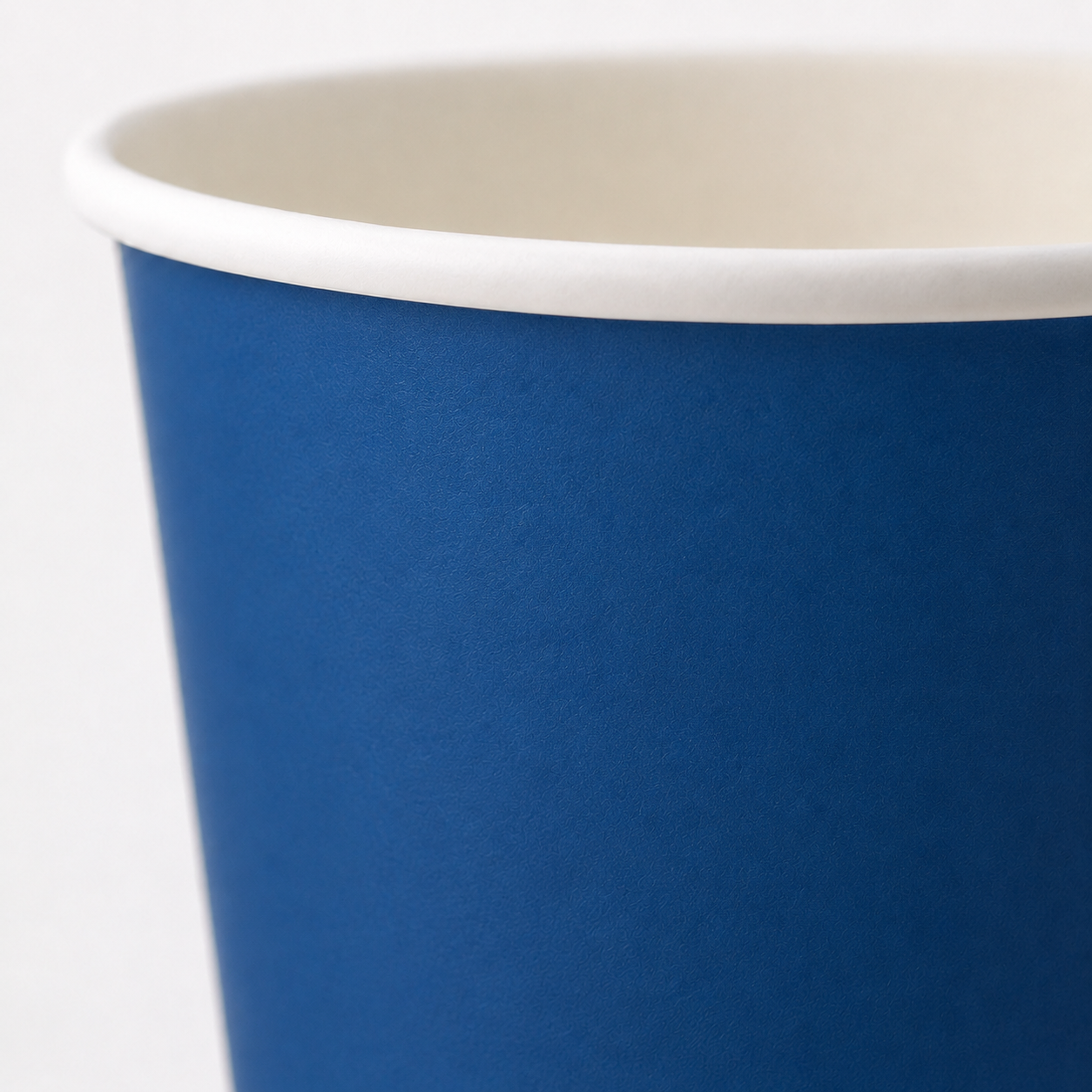 A close-up of a paper cup with a solid blue exterior and a white interior rim, shown against a plain white background.