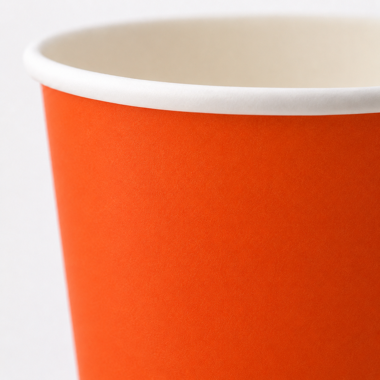 A close-up of a paper cup with a bright orange exterior and a white rim, shown against a plain light background.