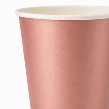 A close-up of a paper cup with a metallic rose gold exterior and a white rim, shown against a plain white background.