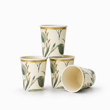 Four paper cups with a botanical pattern of green leaves and gold accents, arranged on a clean white background.