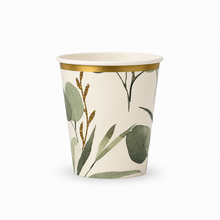 A paper party cup with an off-white background, decorated with green watercolor eucalyptus leaves and gold glittery botanical stems, finished with a metallic gold band around the rim.