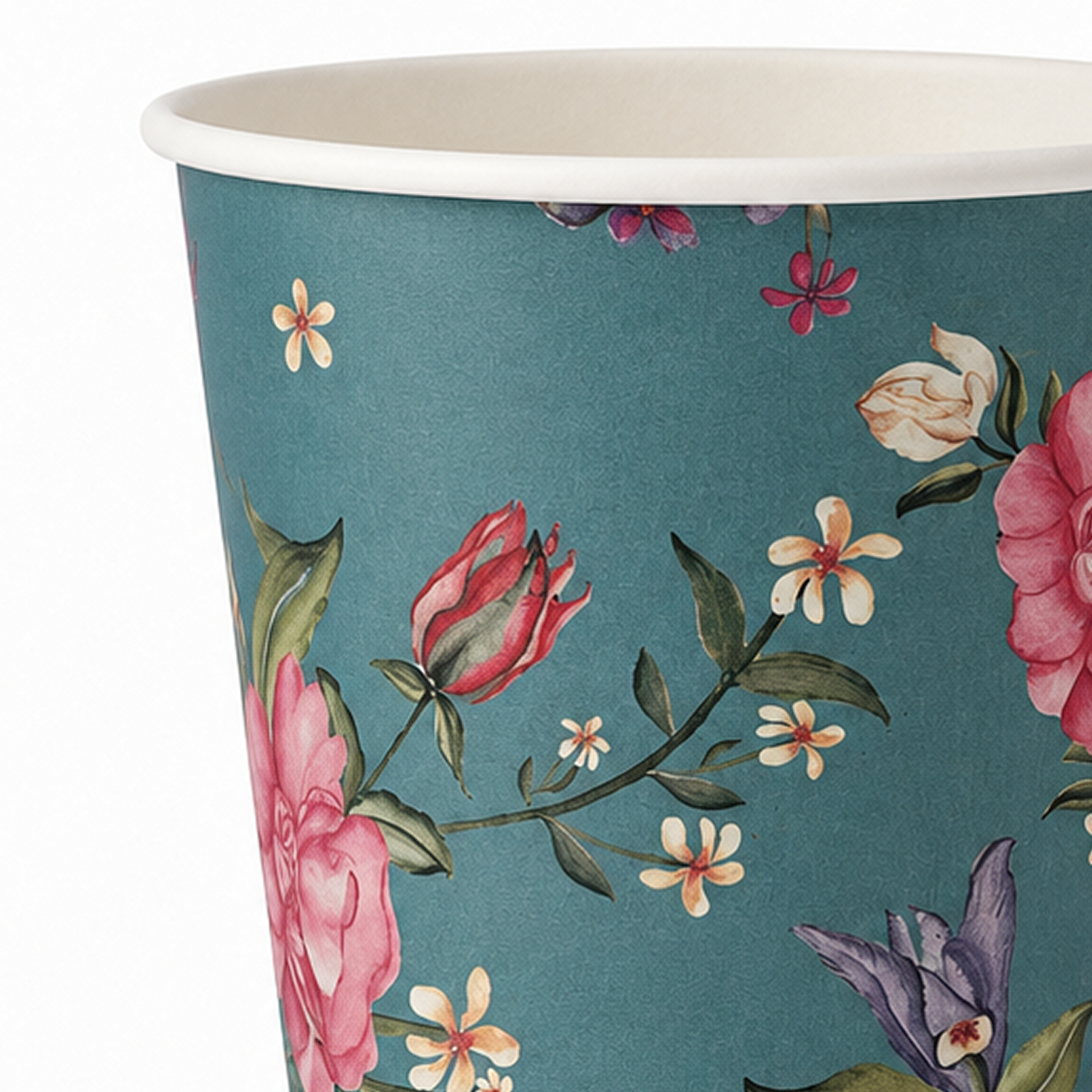 A close-up of a paper cup with a teal background and a floral print featuring pink roses, white flowers, green leaves, and purple blossoms. The rim of the cup is white.