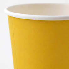 A close-up of a yellow paper cup with a white rim, showing the textured inner wall and white interior.