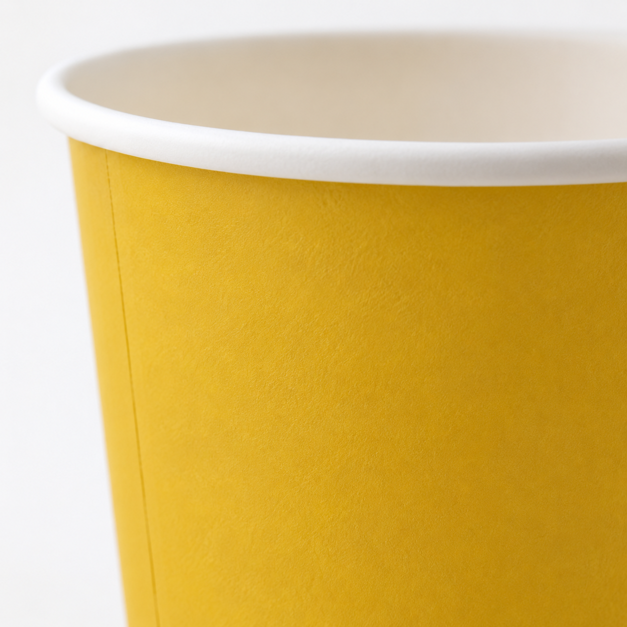 A close-up of a yellow paper cup with a white rim, showing the textured inner wall and white interior.